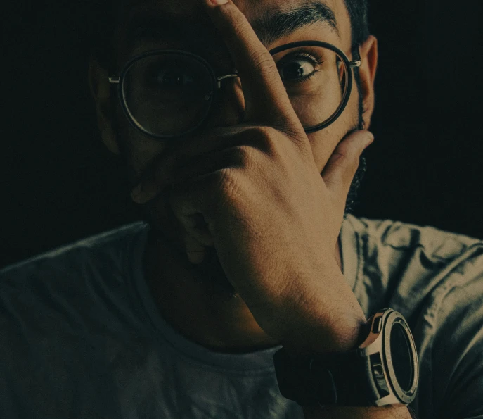 a man in glasses looks up with his hands over his face