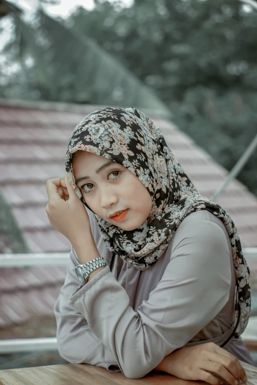 a beautiful young woman in a headscarf sitting at a wooden table