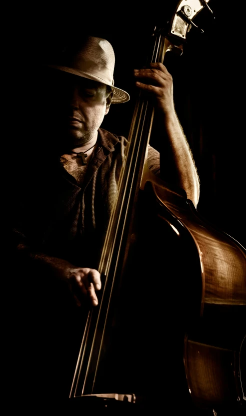 a man is holding on to a cello while wearing a hat