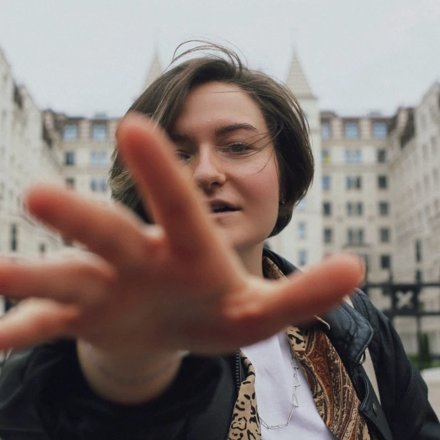 a woman making an odd hand sign while standing in front of some buildings