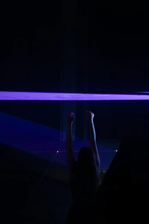 a woman in a dark room pointing to a beam with her arm