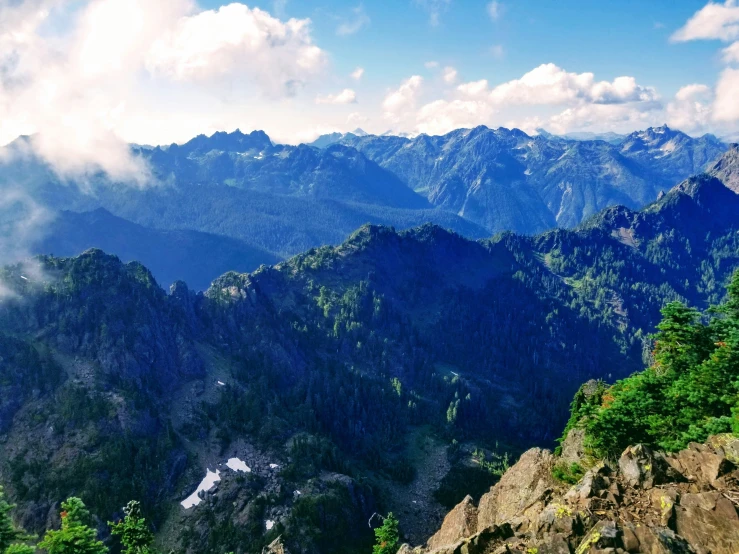 an aerial view of mountains, trees and clouds