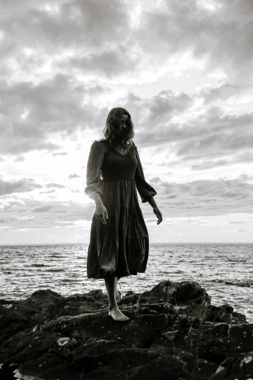 a girl walking along a rocky shore under a cloudy sky