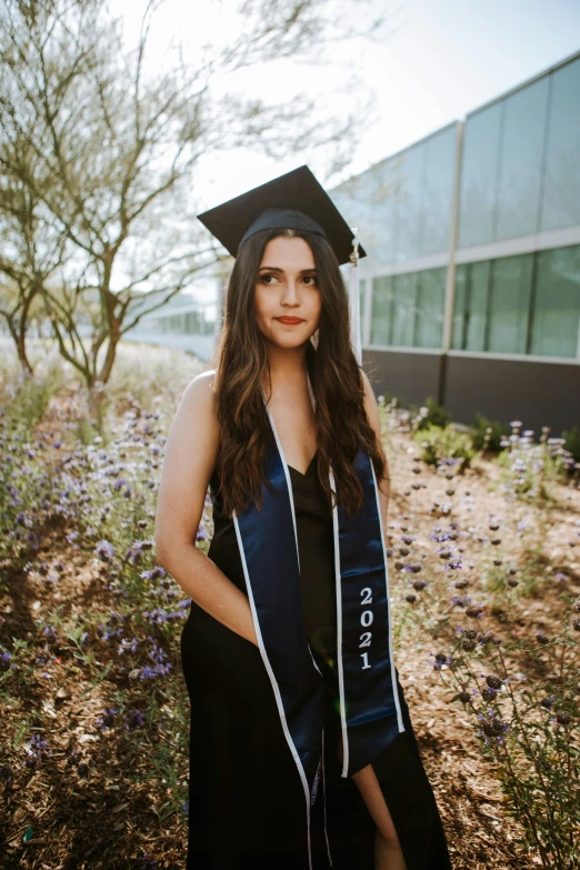 a girl wearing a black cap and gown posing in a garden