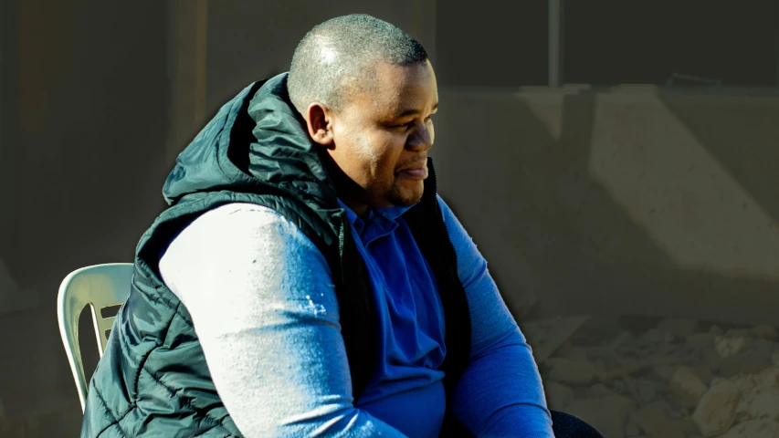 a man wearing a vest and blue sweater looking into the distance