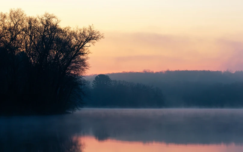 the sun is setting on the trees by the water