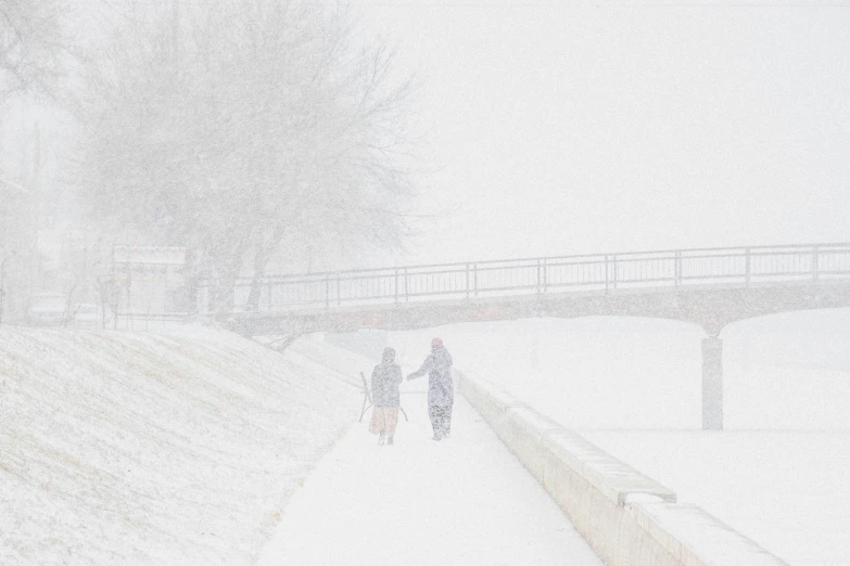 two people walking down a snowy walkway with two on bicycles