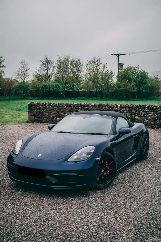 a black sports car parked on gravel in front of a stone wall