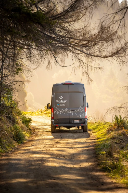 a van driving down a dirt road near trees