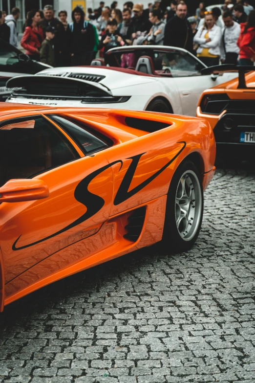 many people looking at orange cars on the street