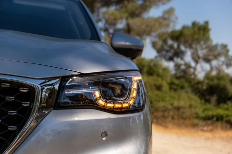 the headlight of a grey car driving on a dirt road