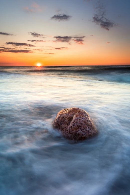 there is a rock sitting on the ocean shore