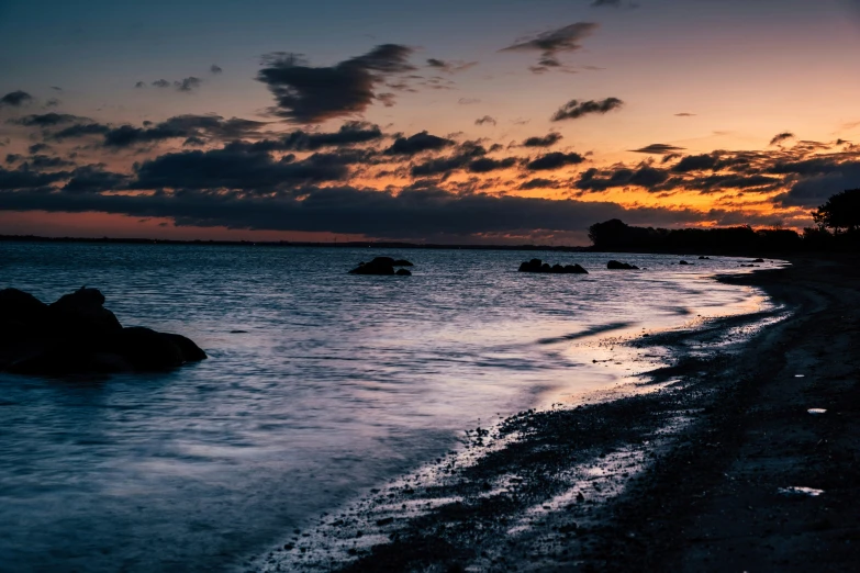 several boulders in the ocean during sunset with clouds overhead