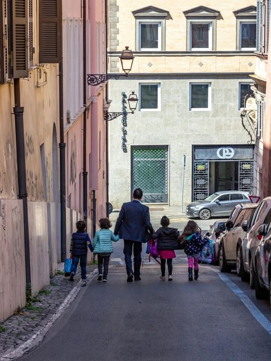 a family is walking down a street past cars