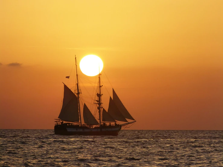 a sailboat with two sails sailing along in front of the sun