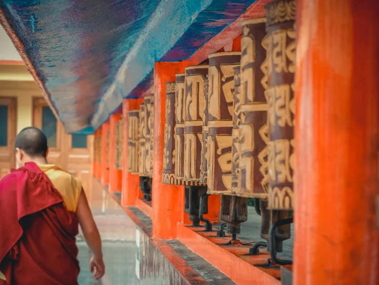 a man wearing a colorful robe walks in between orange columns