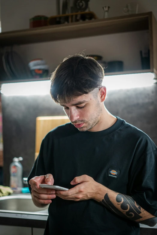 a man stands by a kitchen sink looking at his cell phone