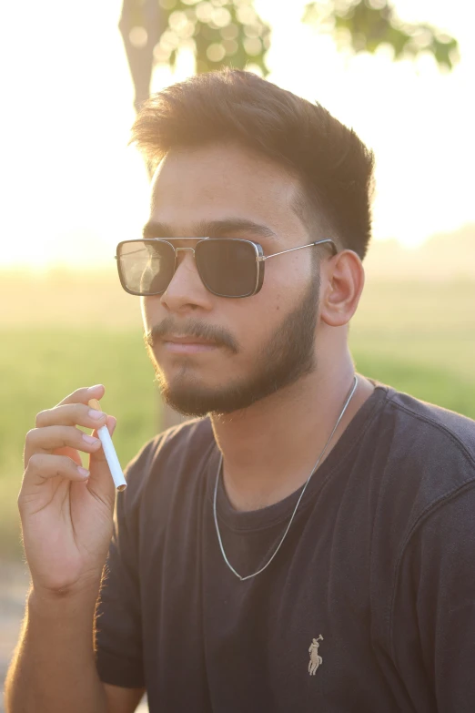 the man wearing sunglasses is holding a cigarette in his left hand