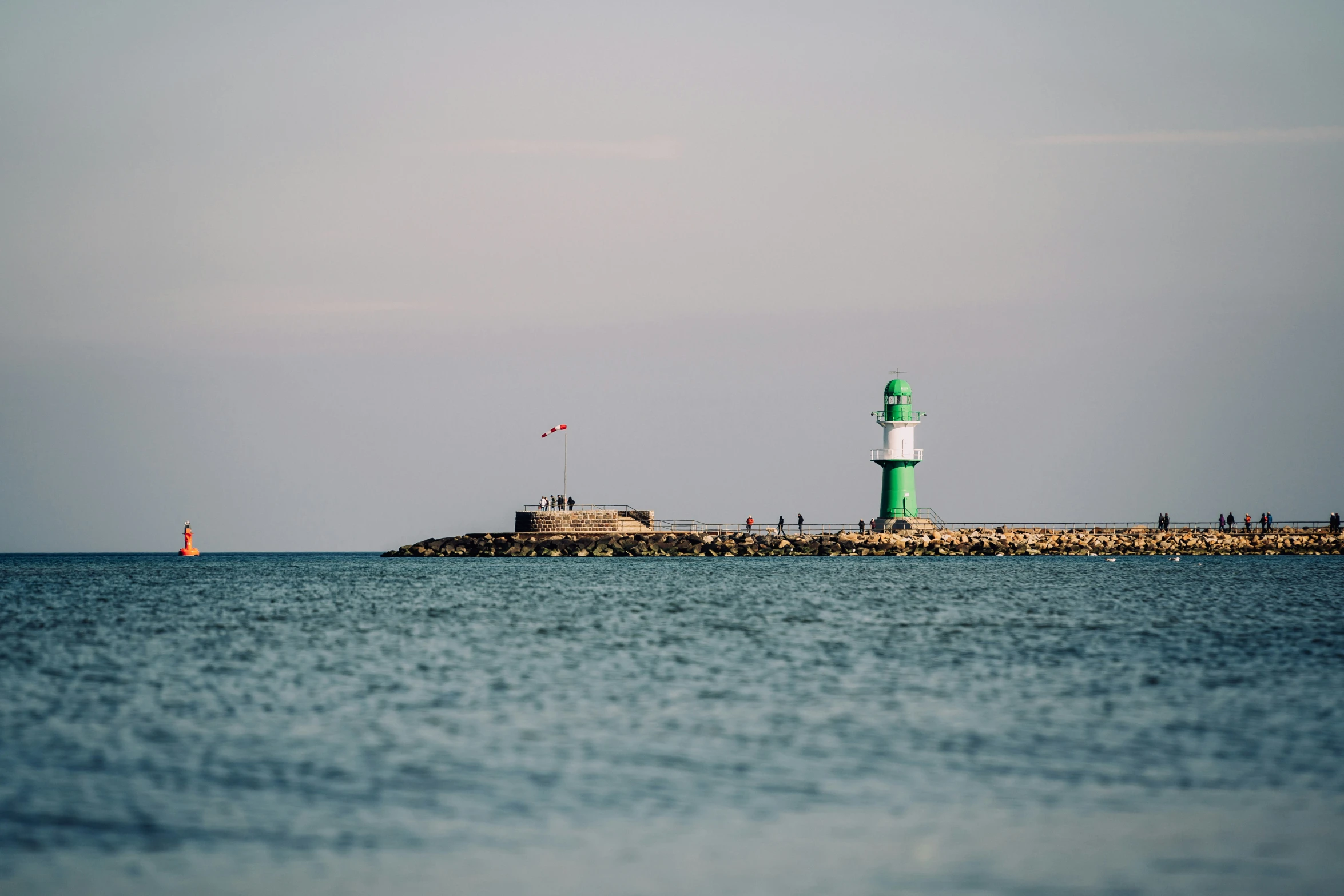 a green light house that is in the middle of water