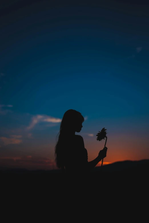 a woman holding a flower in her hand at sunset