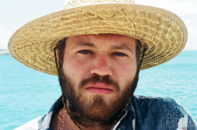 a man with a hat on standing next to a body of water