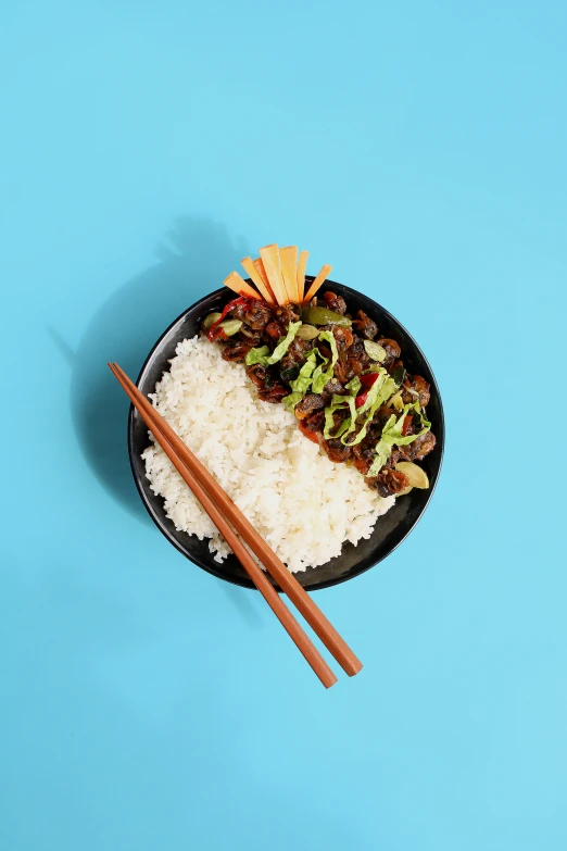 a plate with rice, vegetables and chopsticks next to a container of asian food