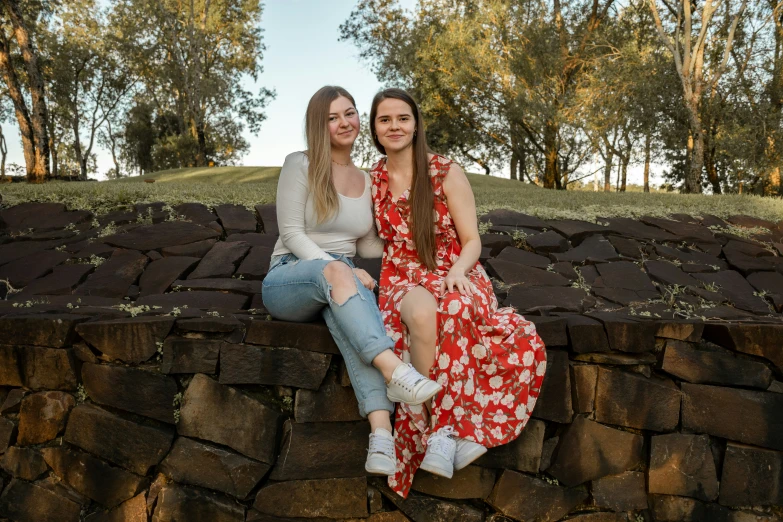 two woman sitting side by side on a stone wall