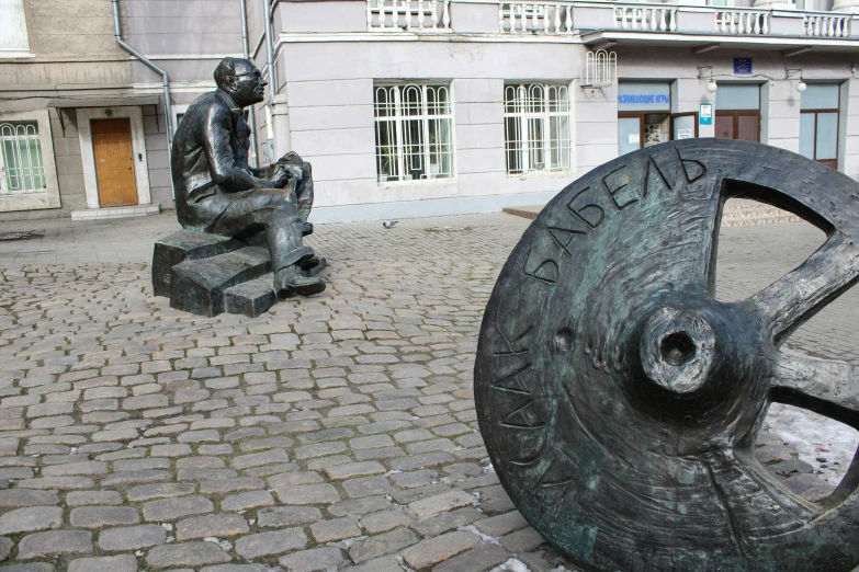 a statue of a man on top of a wheel in the middle of a small brick sidewalk