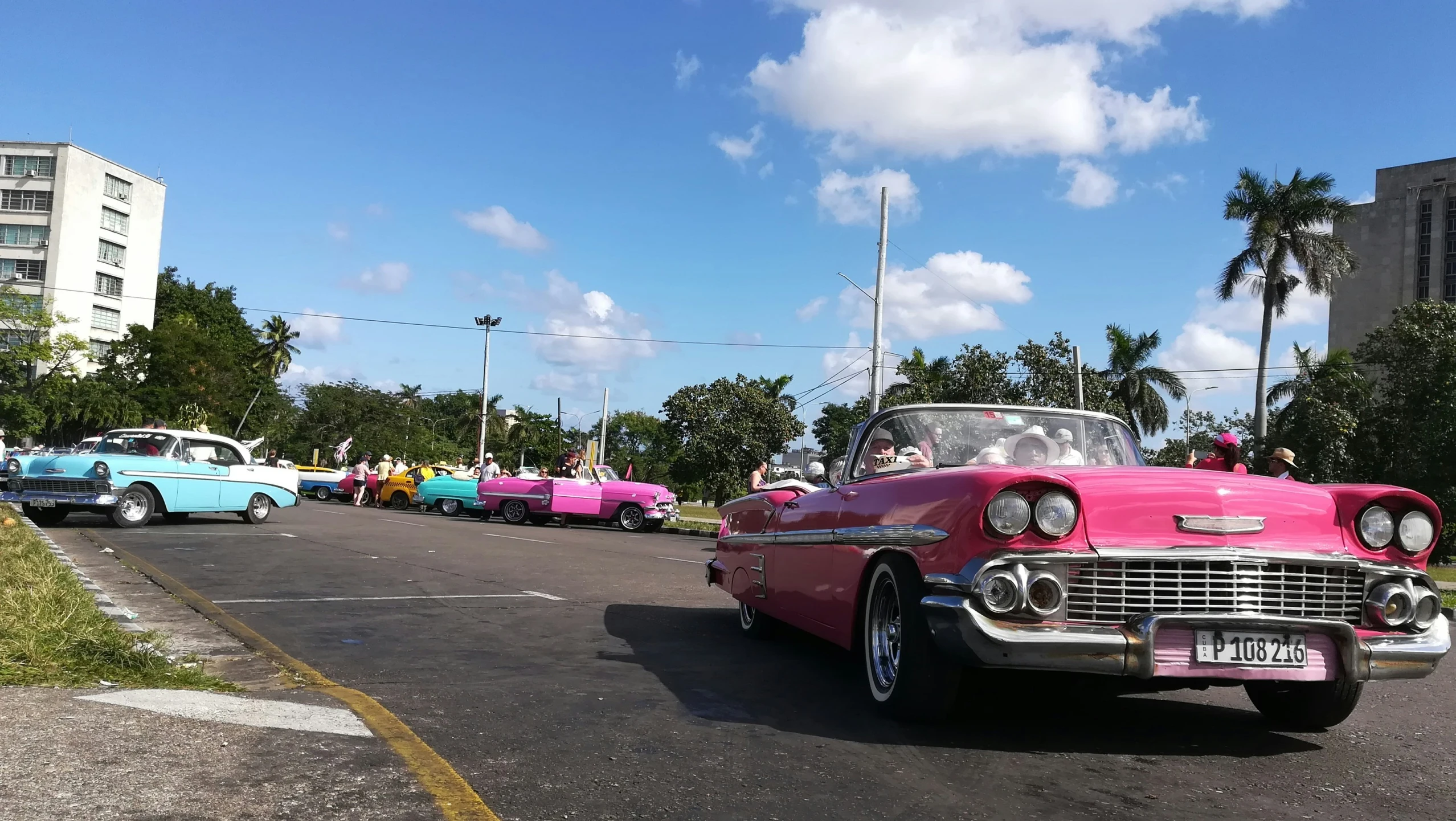 a pink classic car driving past old model cars