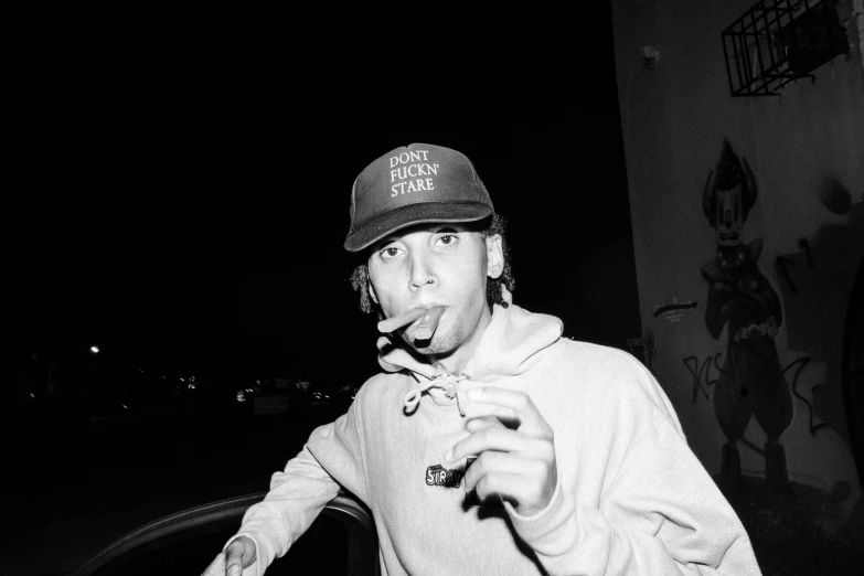 a man standing in front of a black car and smoking a cigarette