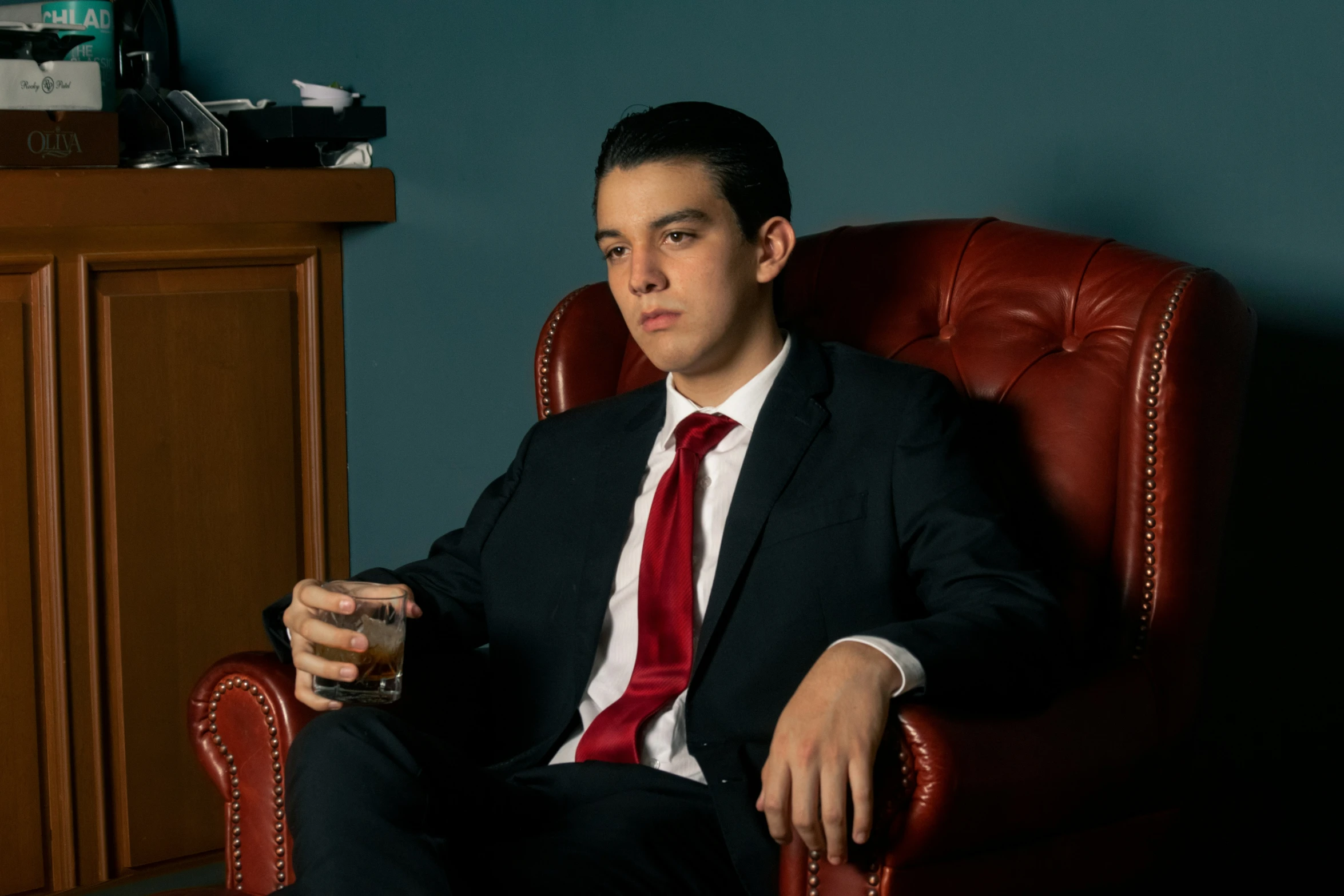 the man sits in a chair holding a drink and looking off