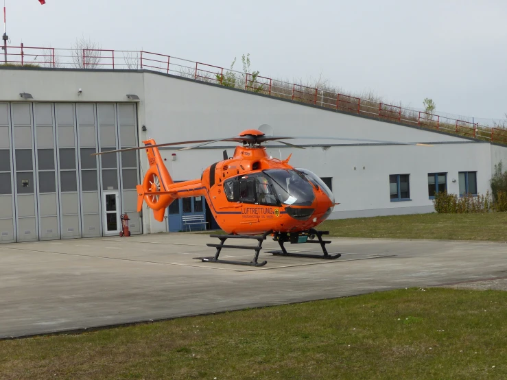 an orange helicopter parked near an industrial building