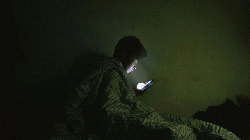 a man sitting in a dark room looking at a laptop