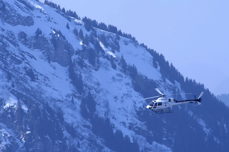 a white and blue helicopter flying next to snow covered mountain