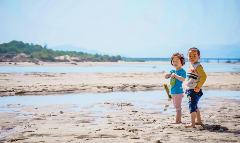 two children stand on a beach and pose for the camera