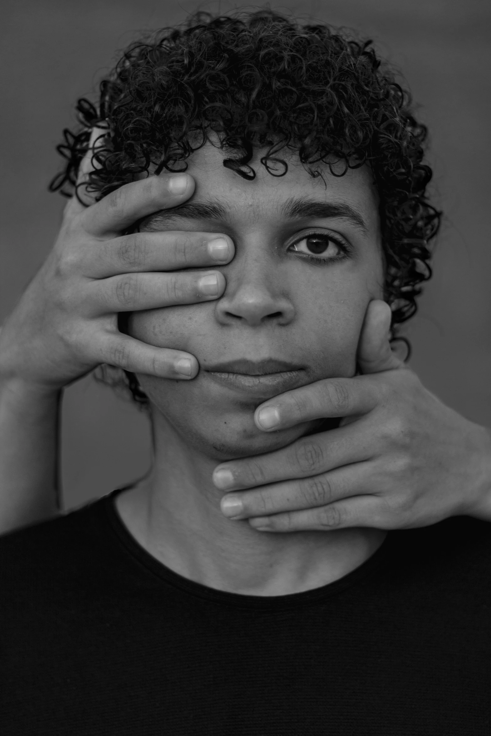 a black and white image of a young man covering his face with both hands