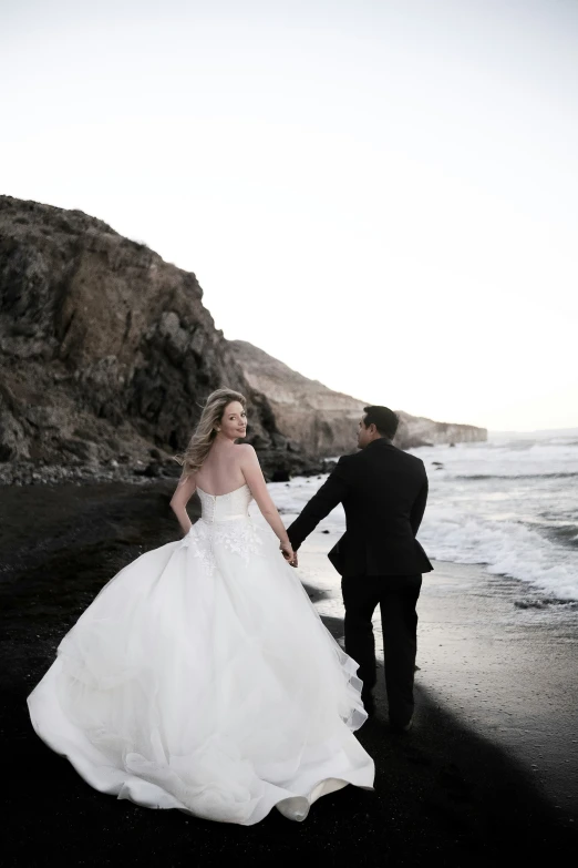 bride and groom hold hands while looking out at the ocean