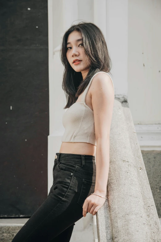 an asian girl standing outside in a crop top and jeans