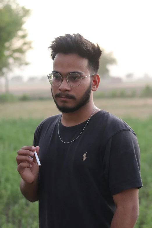 an indian man in black tee shirt and glasses holding cigarette