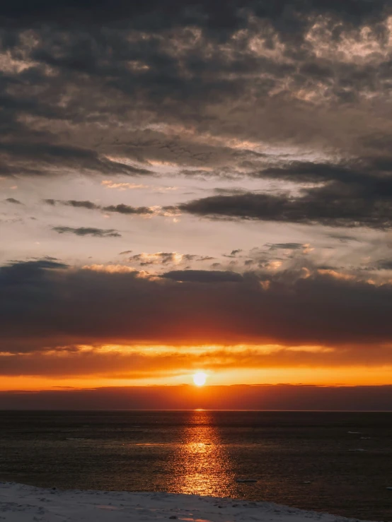 an orange and yellow sunset is seen behind clouds