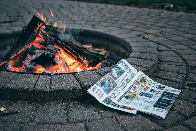 newspapers and fire in the ground next to a fire pit