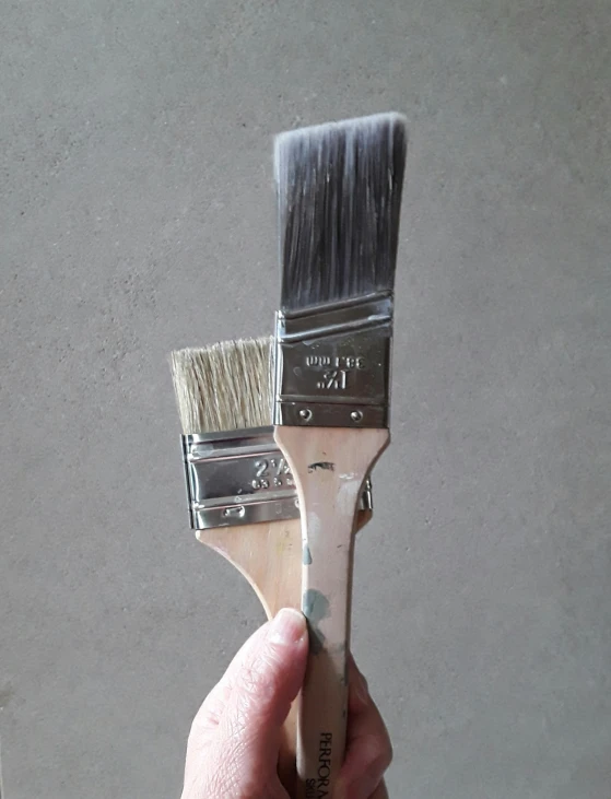 a hand holding a paintbrush that is painted white