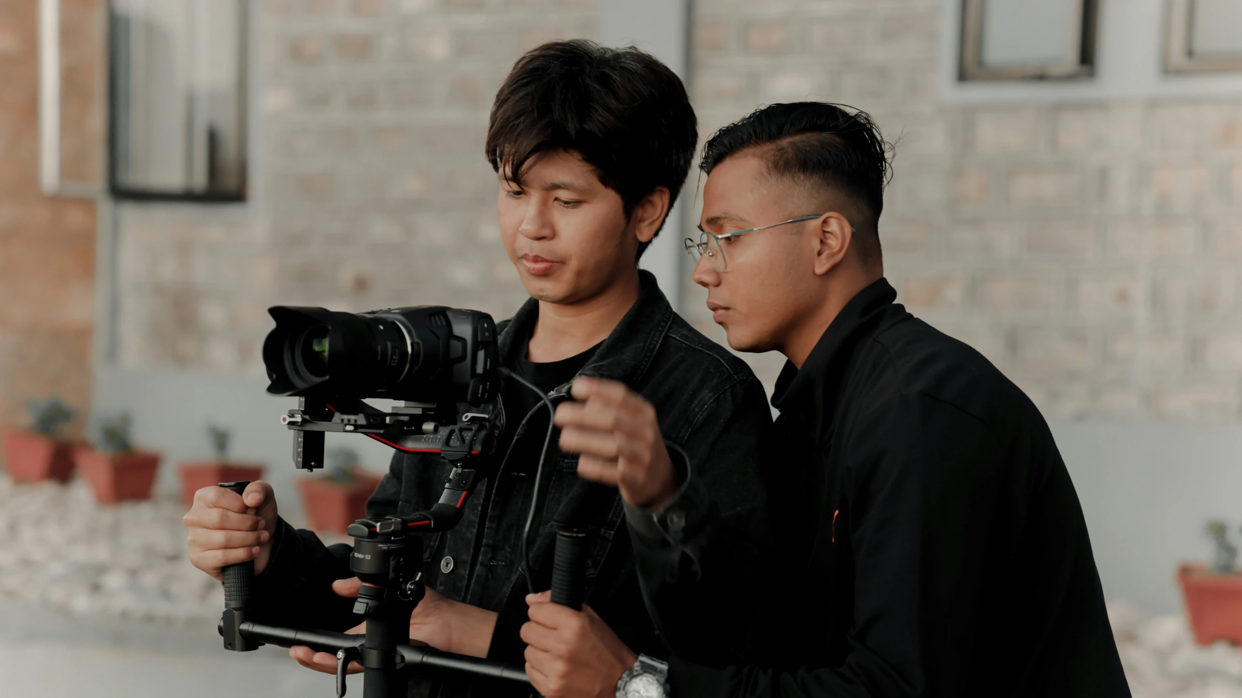 two men holding a camera near a brick wall