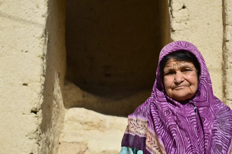 a woman with a purple blanket on standing in front of a brick wall