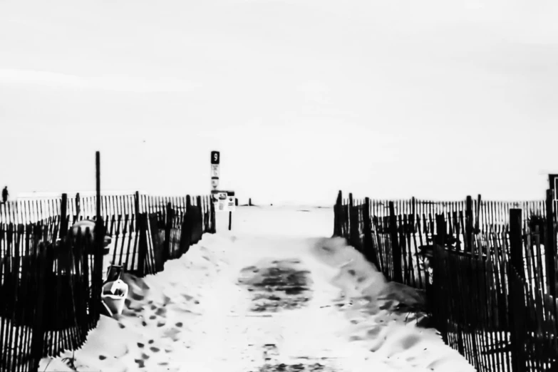 the road is being snowed over by fence posts