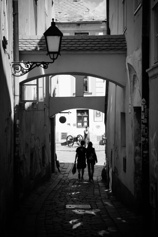 two people walking in an alley near some cars