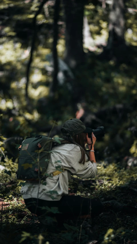 a person with a camera is crouching through the woods