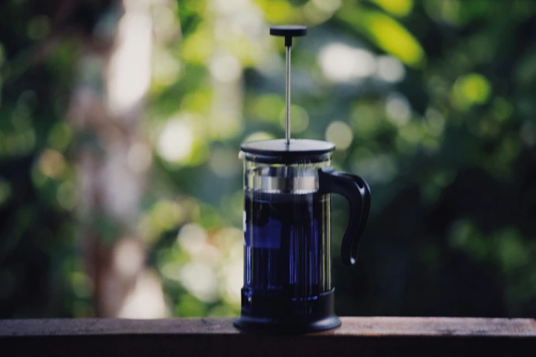 a glass coffee pot with a filter is on a wooden table outside