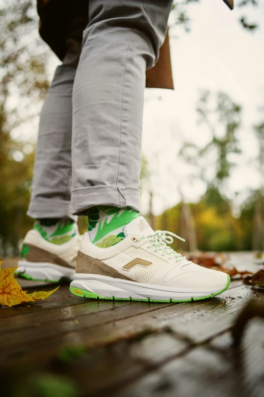 someone in grey jeans standing on a floor wearing white and green tennis shoes