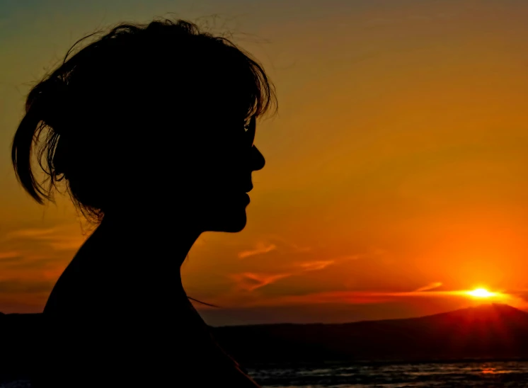 the silhouette of a woman in front of a sunset